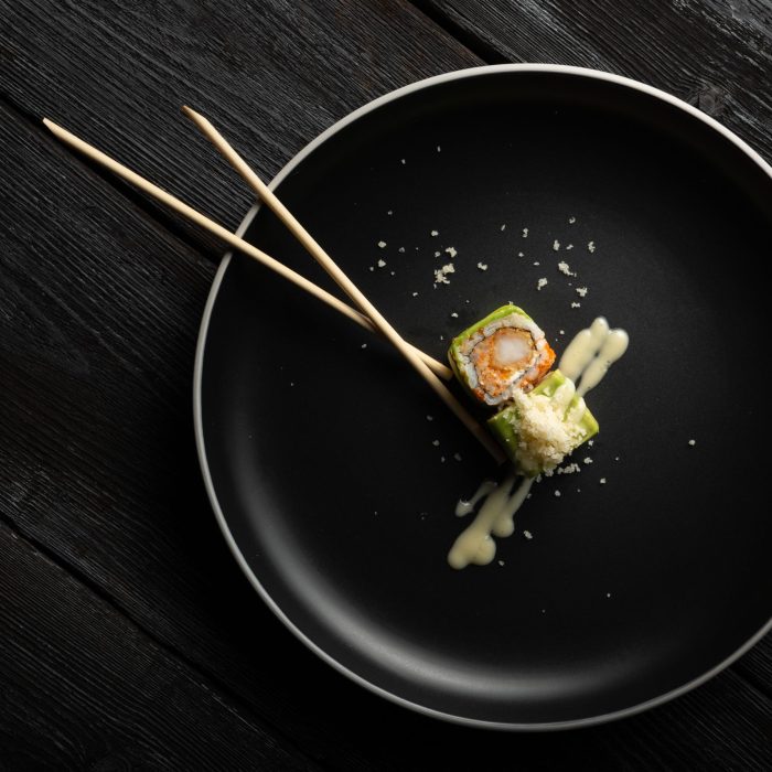 A top view of sushi rolls and chopsticks on a black plate